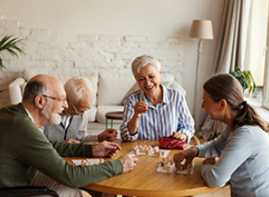 Seniors engaged in a lively game around a table, promoting social interaction and community in a senior living setting.