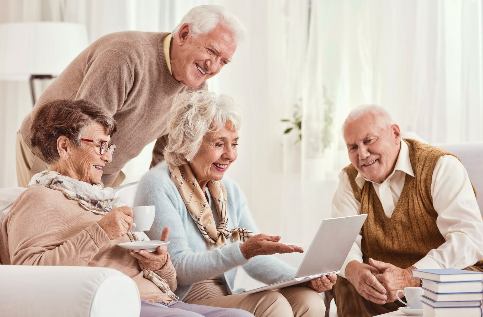 Group of seniors engaging with a laptop, sharing a joyful moment in a cozy living room, highlighting community and social interaction in independent living.